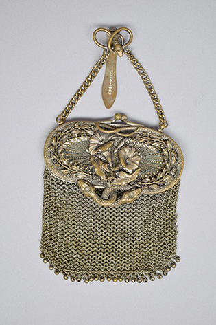 A photograph of a mesh metal purse hanging from a short chain. It has an ornately sculpted silvered brass enclosure in the shape of flowers and snakes.